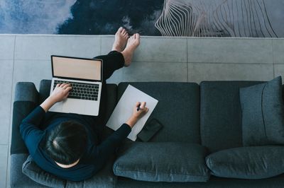 Person working on laptop and writing notes on a couch.