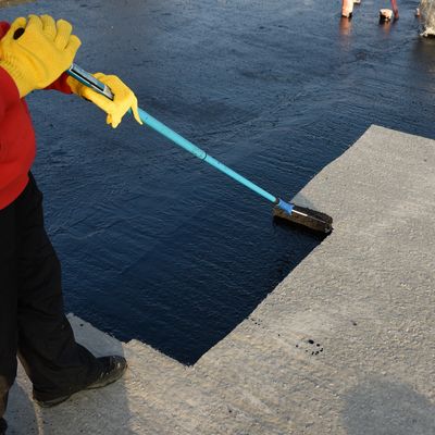 Person applying black waterproof coating on concrete surface with a roller.
