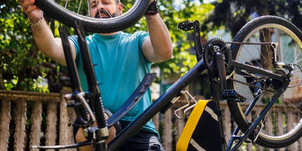 Man repairing a bicycle outdoors on a sunny day.