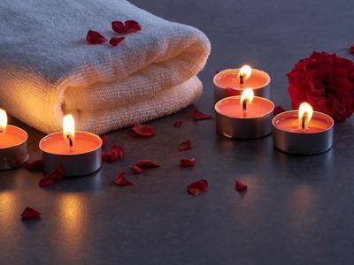 Spa setting with lit candles, white towel, and rose petals.