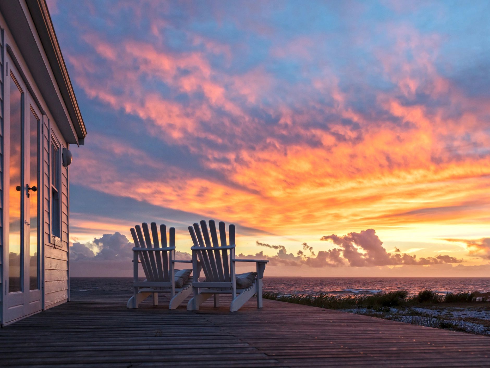 Two chairs on a wooden deck overlooking a vibrant sunset over the ocean.