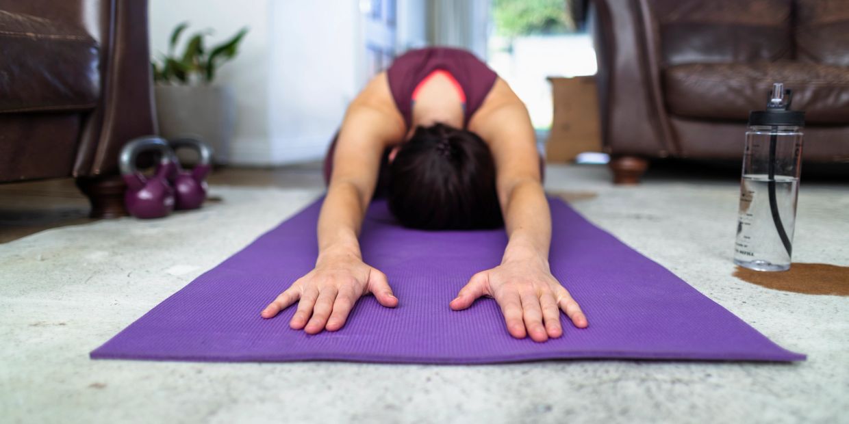 Person stretching on a purple yoga mat indoors.