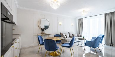 Bright modern living room with blue chairs and sofa, round dining table, and large window with curtains.