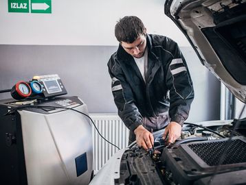 Mechanic working under a car hood in a repair shop.
