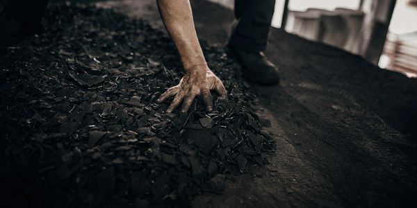 A person touches a pile of dark, broken pieces on the ground in a dimly lit space.