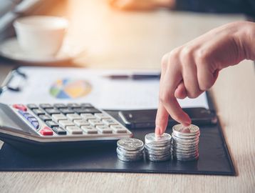 Hand stacking coins beside a calculator and financial chart.