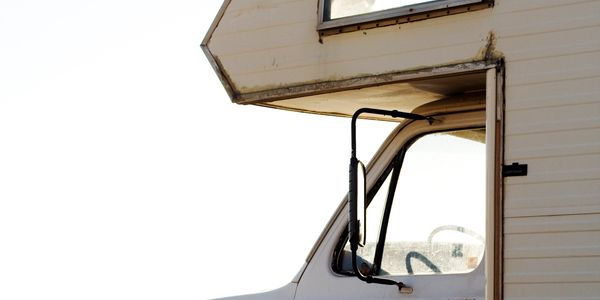 Side view of a white RV with a window and door open under bright light.