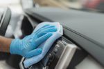 Person cleaning a car dashboard with a cloth and gloves.