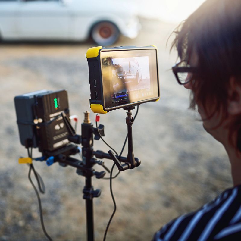 Over the shoulder shot of a focused young man shooting a scene with a state of the art video camera outside on a beach during the day