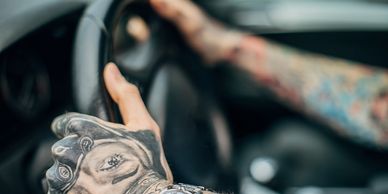 Two tattooed arms holding a car steering wheel