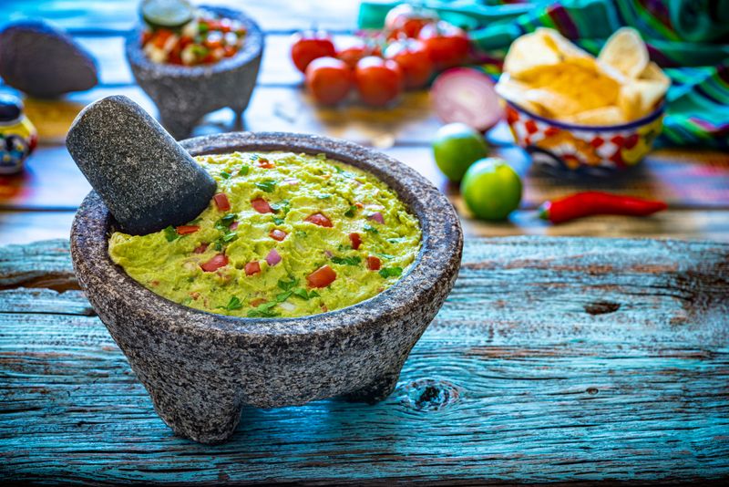 Guacamole Mexican avocado recipe on blue rustic board with ingredients in background