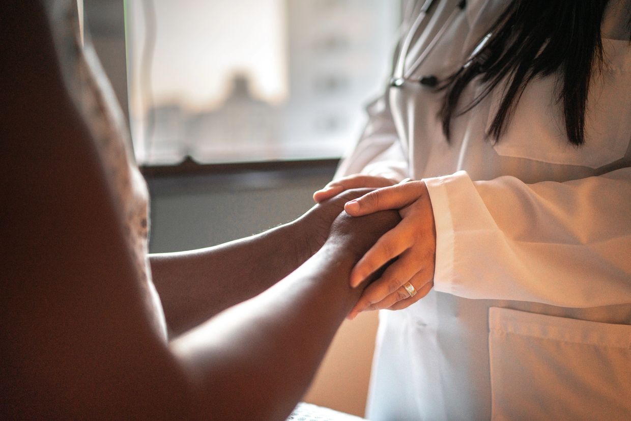 A doctor gently holds a patient's hands, offering comfort and support.