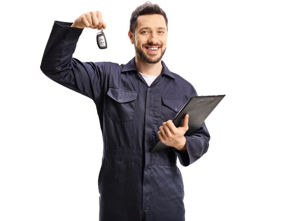 Smiling mechanic holding car keys and clipboard.
