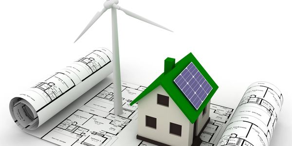 Model eco-friendly house with solar panels and wind turbine on architectural plans.