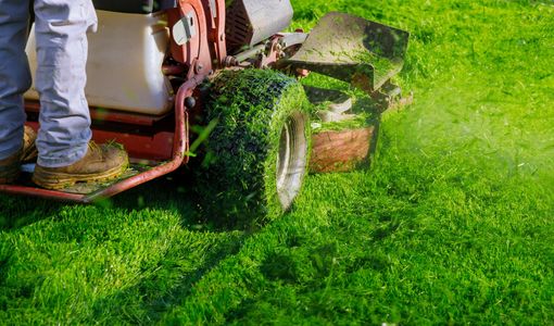 Three lawn mowers on a green field under a blue sky.