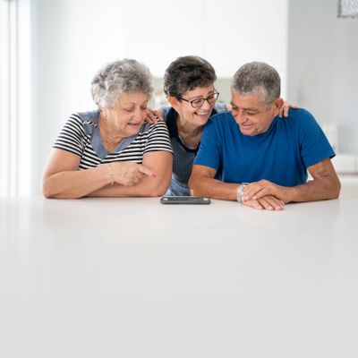 Three older adults smiling and looking at a smartphone together.