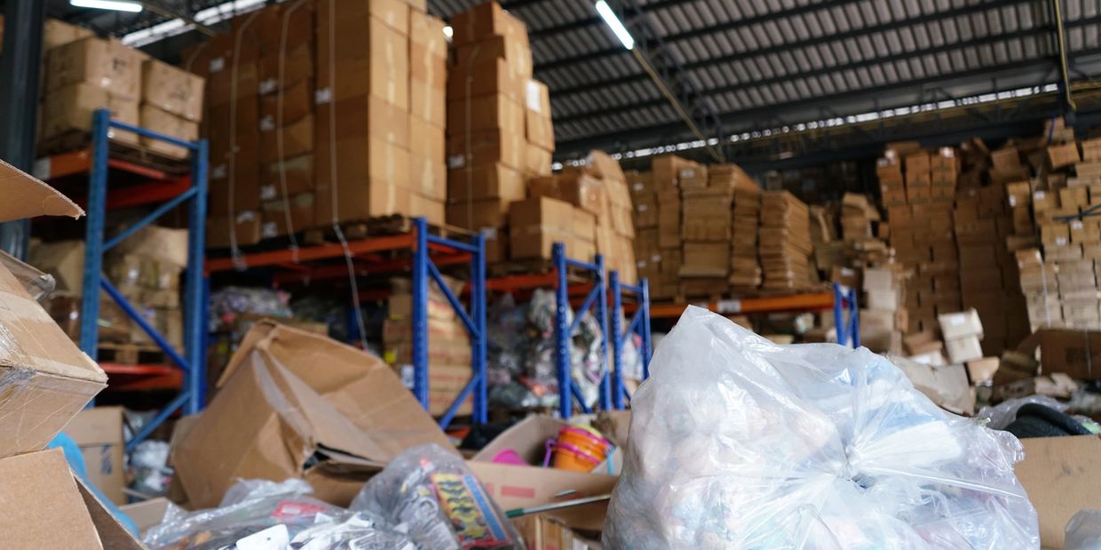 A cluttered warehouse filled with cardboard boxes and plastic bags.