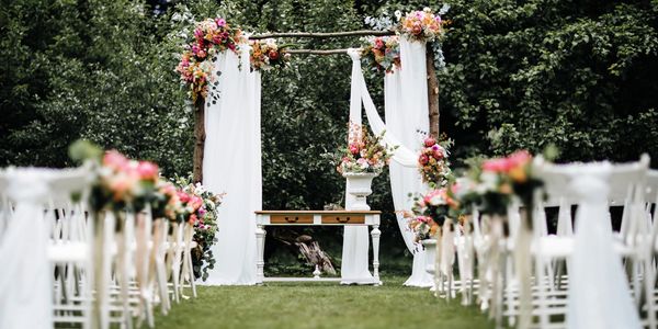 Outdoor wedding setup with wooden arch floral decorations and white padded resin chairs. All party supplies you need to create a special event planning.