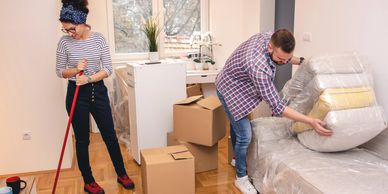 Couple unpacking and cleaning in a new home with boxes and furniture.