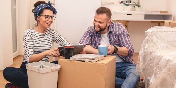 A couple enjoying coffee while sitting on the floor among moving boxes in a bright room.