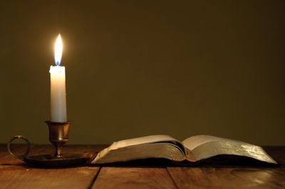 An open book beside a lit candle on a wooden surface.