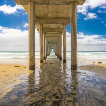 The iconic pilings of Scripps Pier in La Jolla, California on a sunny day with fluffy clouds