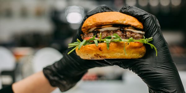 Hands in black gloves holding a gourmet burger with fresh greens.