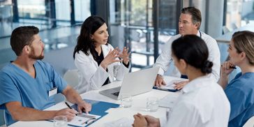 Medical professionals in a meeting discussing patient care around a table.