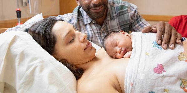 Postpartum bonding featuring a newborn resting on their mother’s chest with dad looking. Birth doula