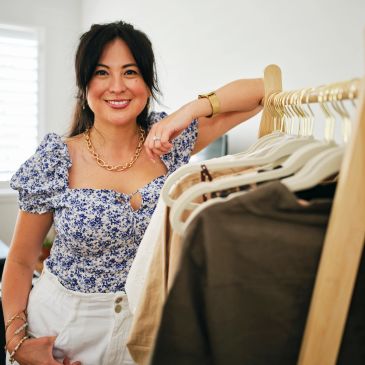 Woman smiling beside clothing rack.