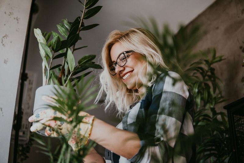 A happy woman enjoys time at her home, She waters one of her plant arrangements with a watering can.