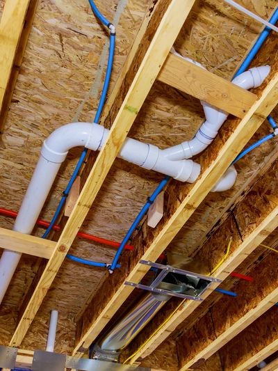 Exposed ceiling with wooden beams and white plumbing pipes.