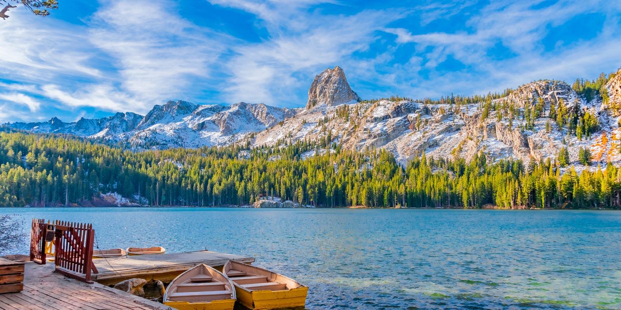 Boats docked by a serene mountain lake with snowy peaks and blue sky.
