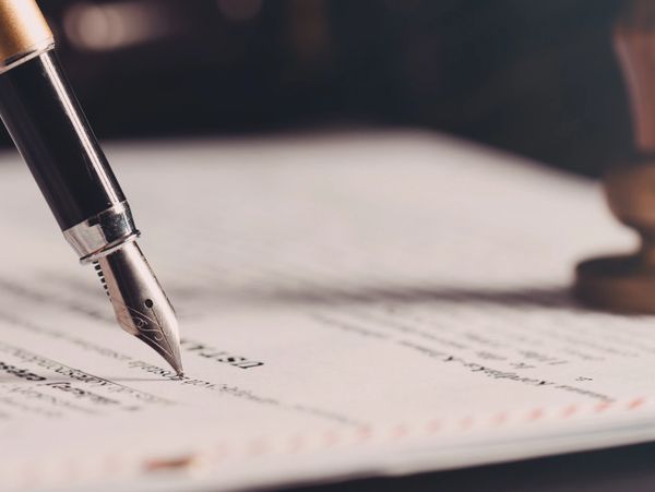 Close-up of a fountain pen on a document with a wax seal stamp nearby.