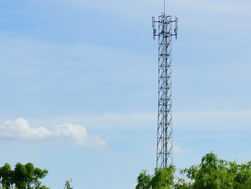 A tall communication tower rising above green trees under a clear blue sky.