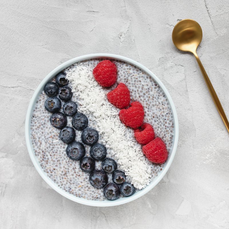 Overnight chia seed pudding with fresh blueberries, raspberries and coconut flakes in a bowl with golden spoon Copy space, top view. Breakfast, superfood and vegan food concept. Gray background