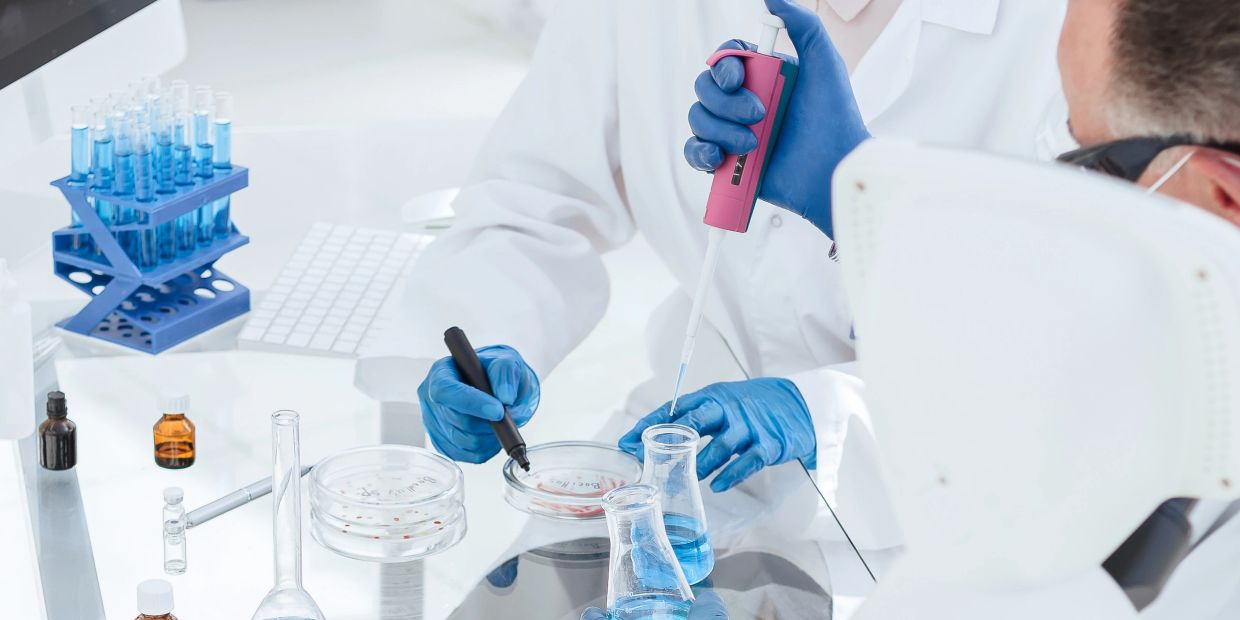 Scientist using pipette and marking petri dish in lab.