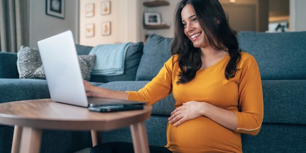 Pregnant woman smiling while using a laptop at home.