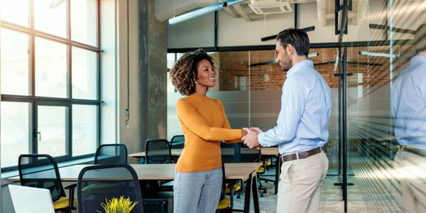Two colleagues shaking hands in a bright office space.