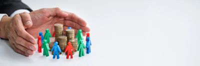 Hands protect stacked coins surrounded by colorful toy figures symbolizing financial security.