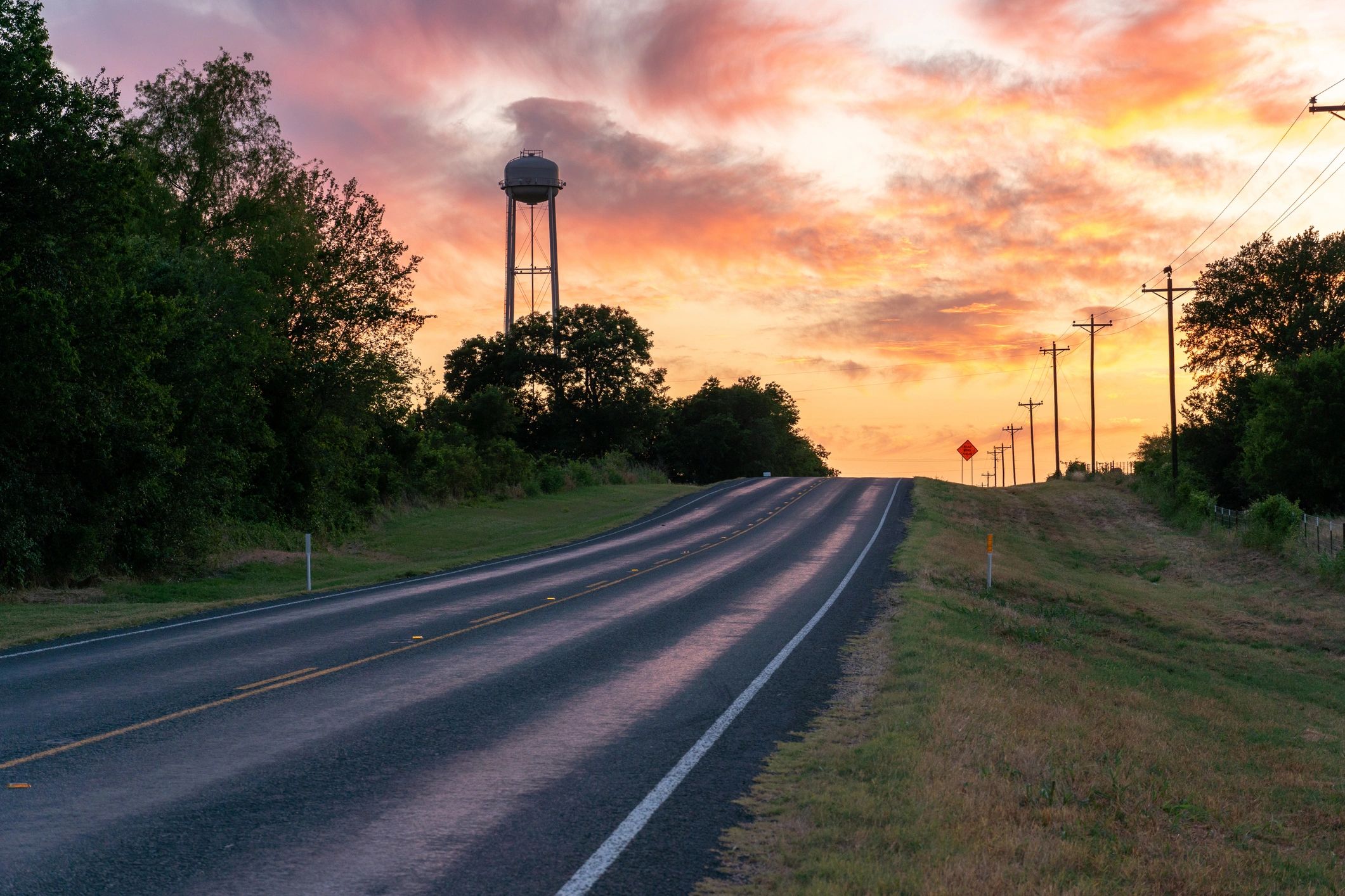Road at sunset with water tower and power lines.