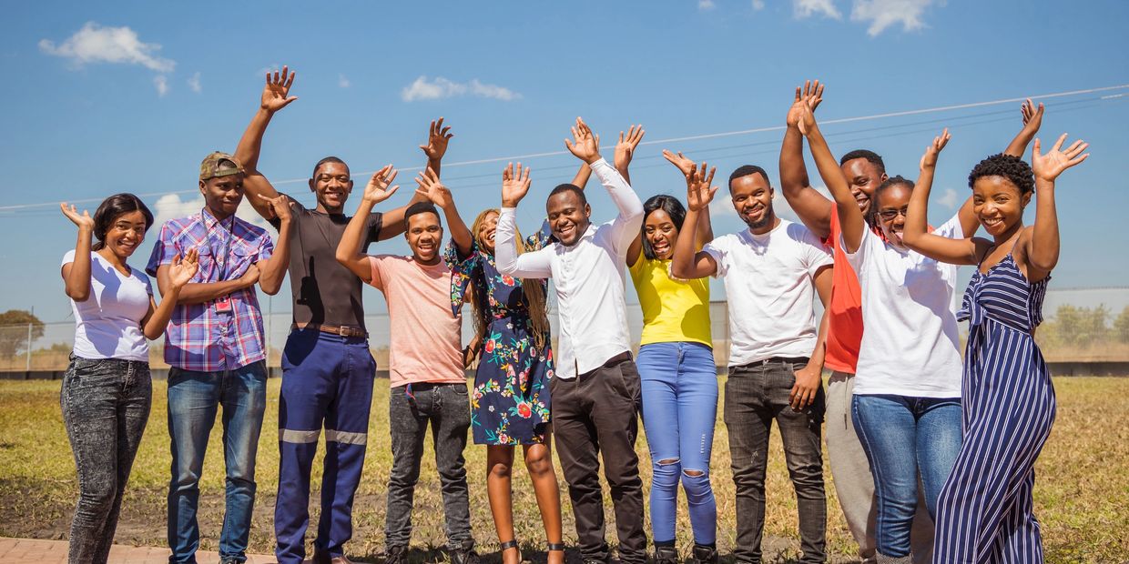 A group of cheerful young adults raising their hands outdoors on a sunny day.