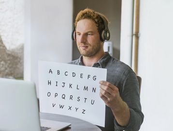 Man with headphones holding paper displaying alphabet letters during online session.