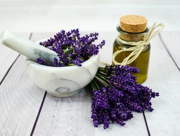 Lavender flowers with a marble mortar and pestle and a small bottle of essential oil.