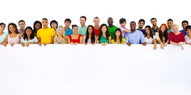 Diverse group of young adults standing behind a large blank white banner, smiling.