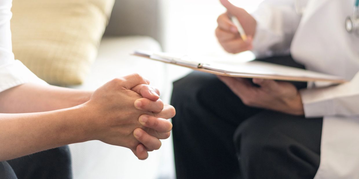 Patient consulting with a doctor holding a clipboard during a medical appointment.