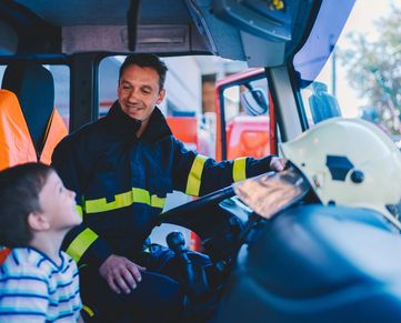A firefighter talks to a child inside a fire truck.
