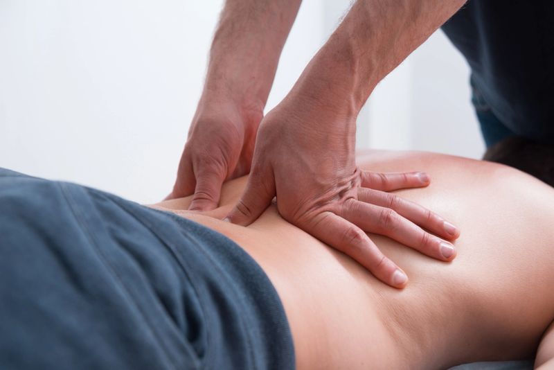 Physical therapist pressing or pushing on lower back maknig deep massage.
