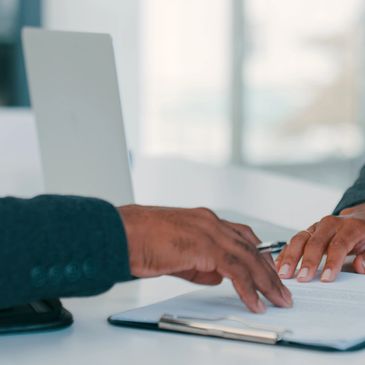 Two people reviewing a document together at a desk with a laptop.