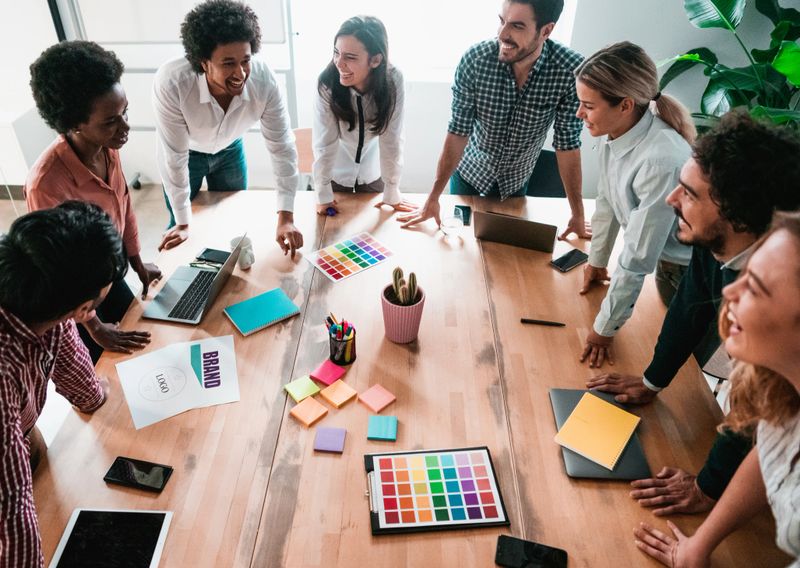 Group of young business people working together in creative office. Multi-ethnic group of creative people on a business meeting in modern office. Cheerful creative team standing around conference table in board room.